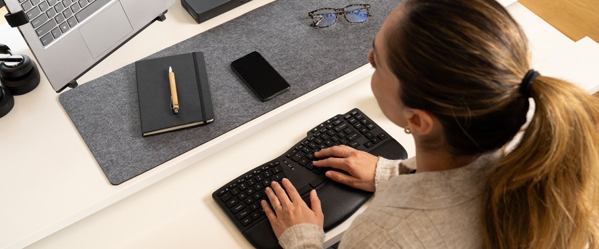 A woman types on a Kensington ergonomic keyboard at a neatly organized desk.