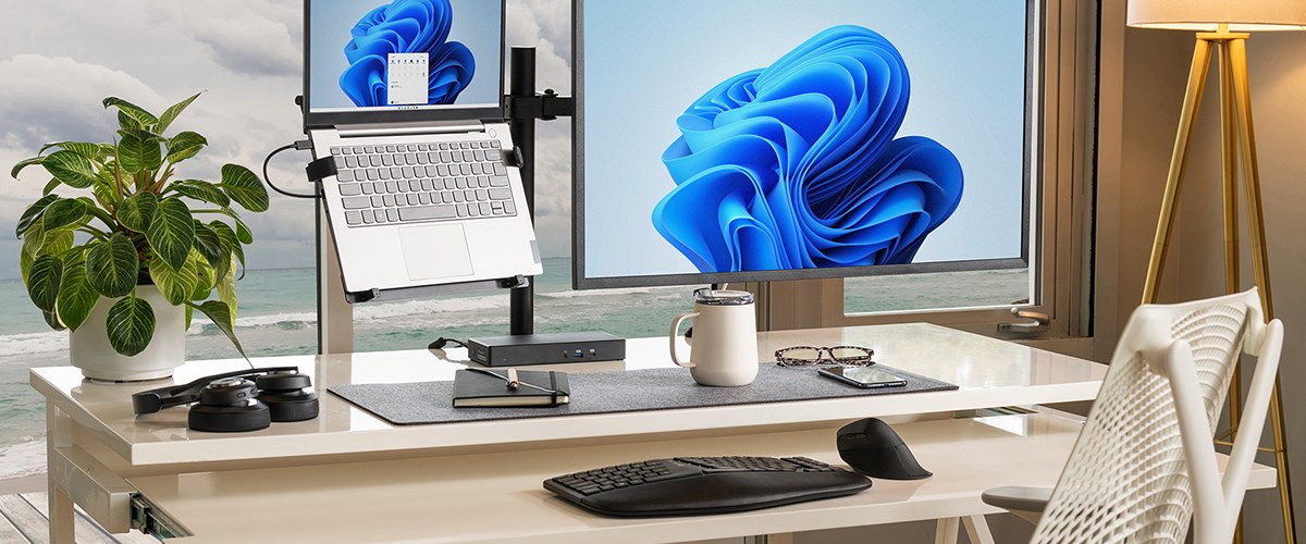 home office setup featuring a desk with a large monitor displaying a blue abstract design, a laptop mounted on a stand, and a variety of office accessories. The desk includes a wireless keyboard, mouse and a pair of headphones.