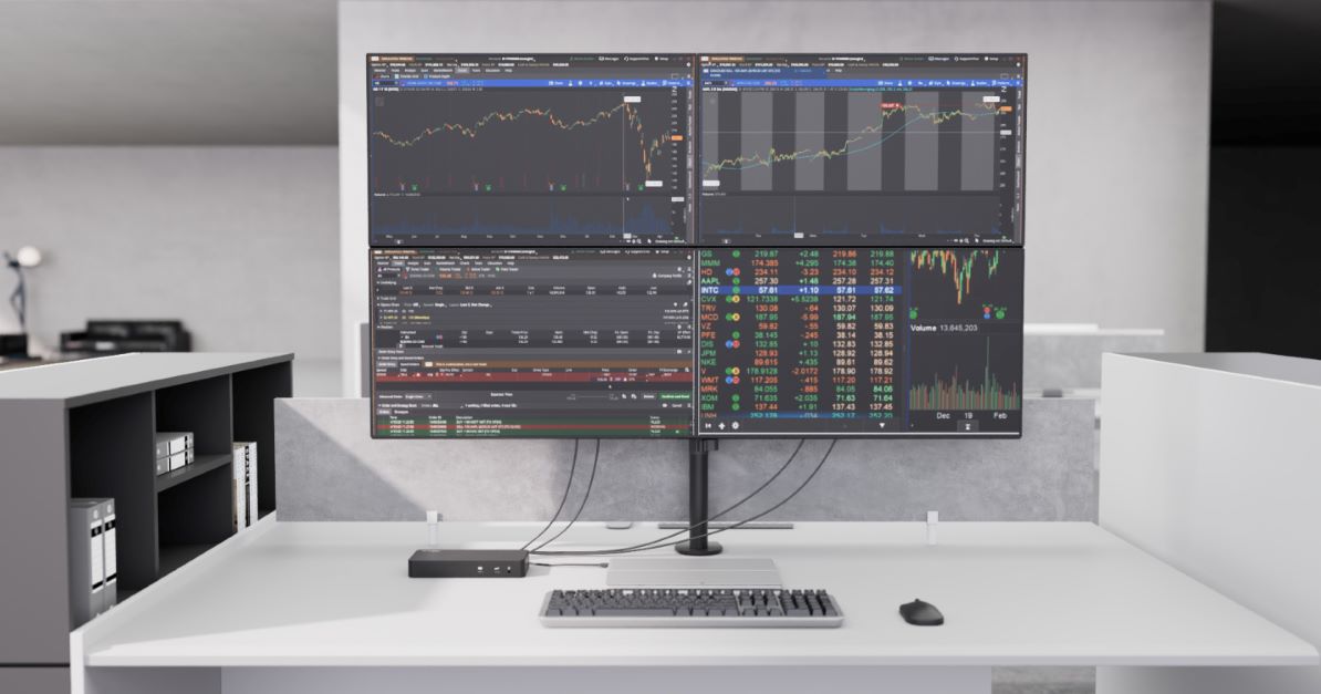  A desk setup with four monitors displaying financial data, connected via a docking station.