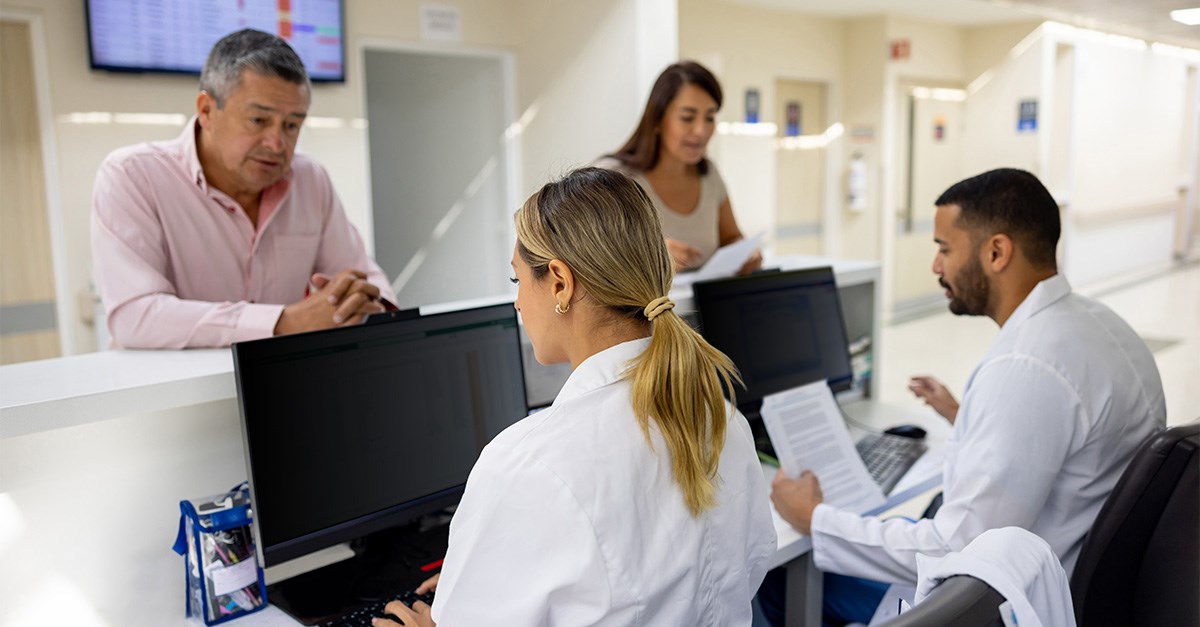 Staff at a healthcare reception desk use privacy screens to prevent unauthorized viewing of sensitive information.