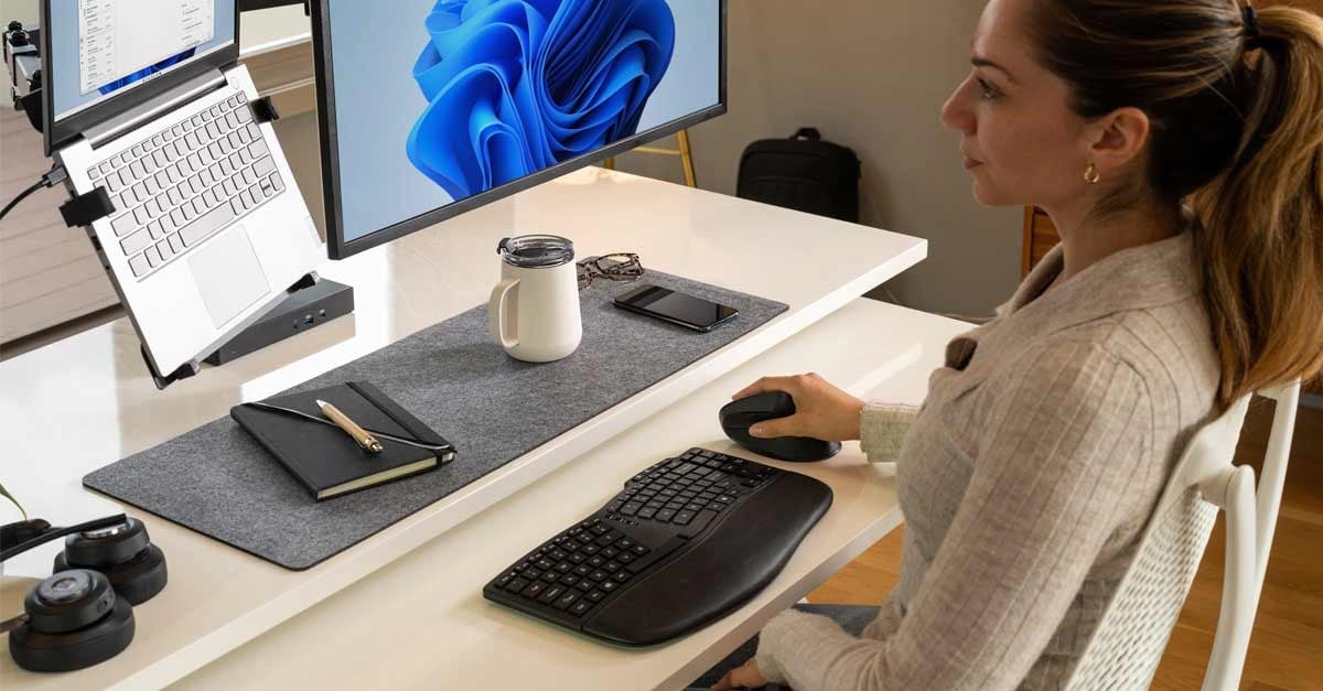 A woman uses an ergonomic Kensington keyboard and vertical mouse at a tidy desk with a large monitor.