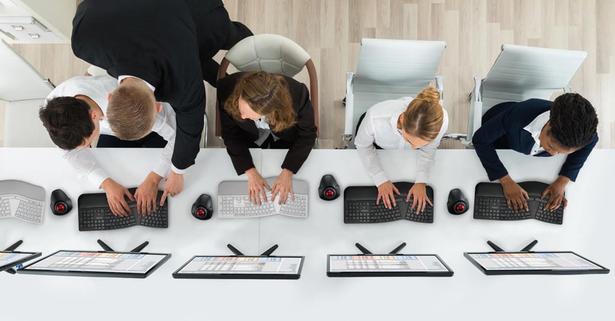 People working, each using ergonomic keyboards and Kensington trackballs in a shared workspace.