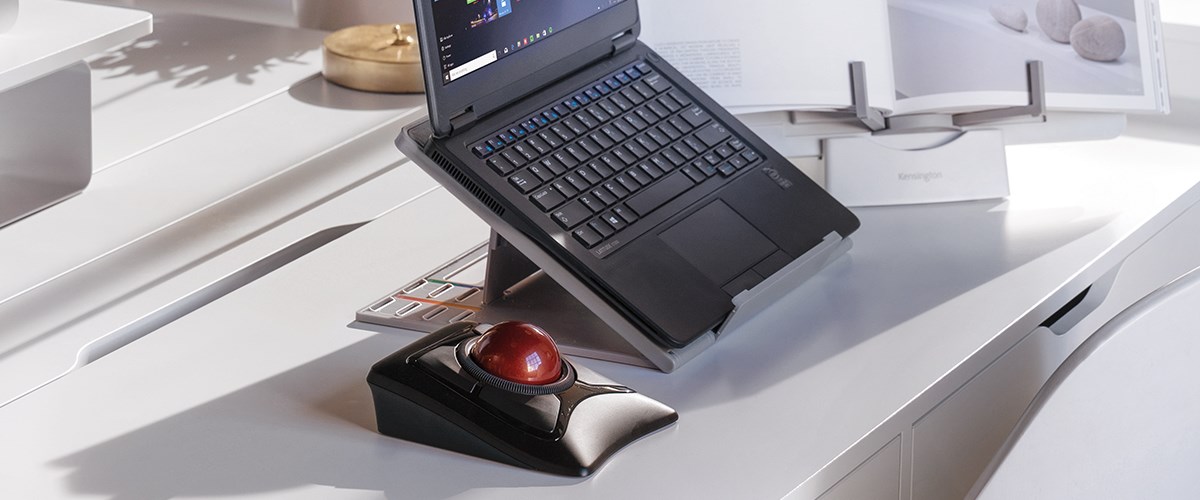 A laptop on a stand, paired with an Expert Mouse Wireless Trackball on a white desk.