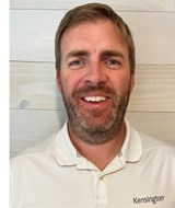 Donovan Shaughnessy, in a white Kensington polo shirt, smiling in front of a wood-paneled wall.