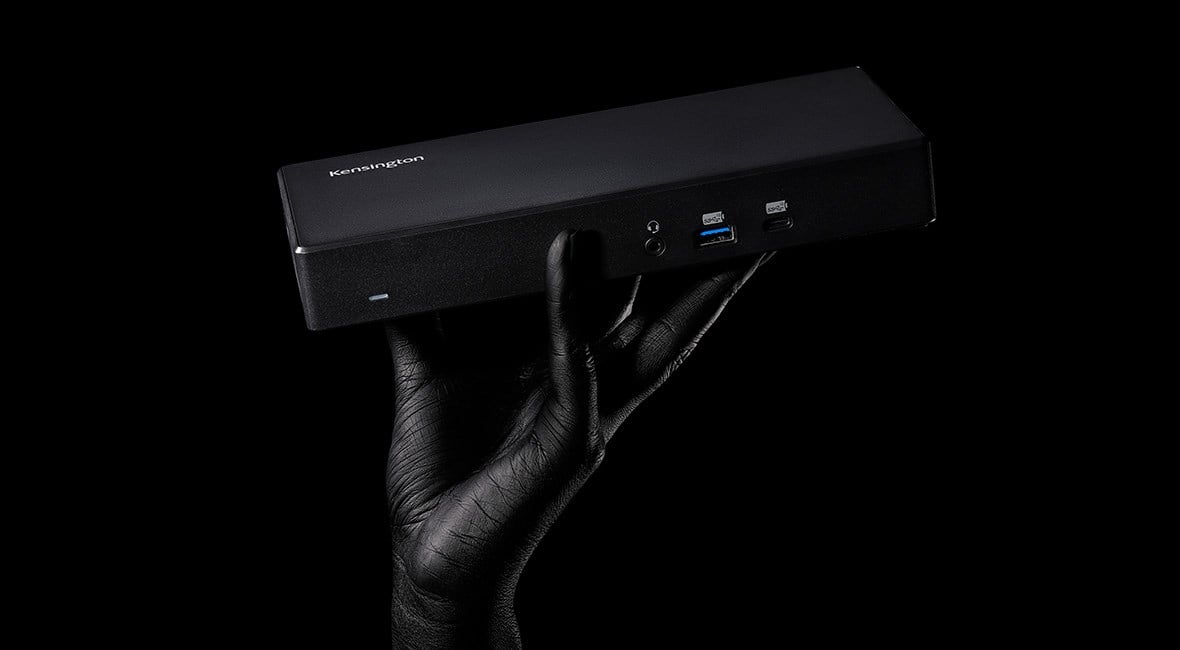 Una imagen oscura que muestra un Docking Station 4K doble SD4782P EQ con puerto USB-C y USB-A de Kensington sostenido por una mano humana. 