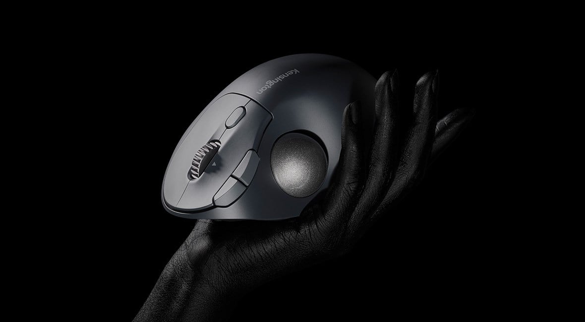 Un trackball de Kensington EQ negro sostenido por una mano sobre un fondo oscuro. 