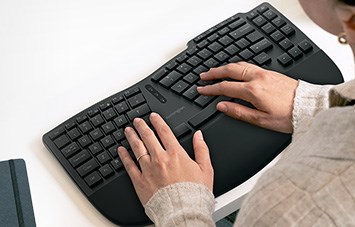 Woman typing with the Pro Fit® Ergo KB675 EQ TKL Rechargeable Keyboard.