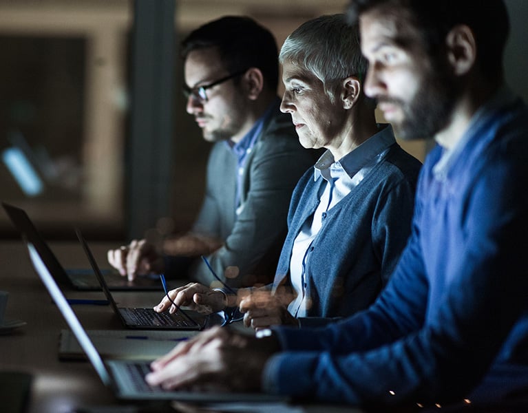 3 people in office using laptops with bright screens.
