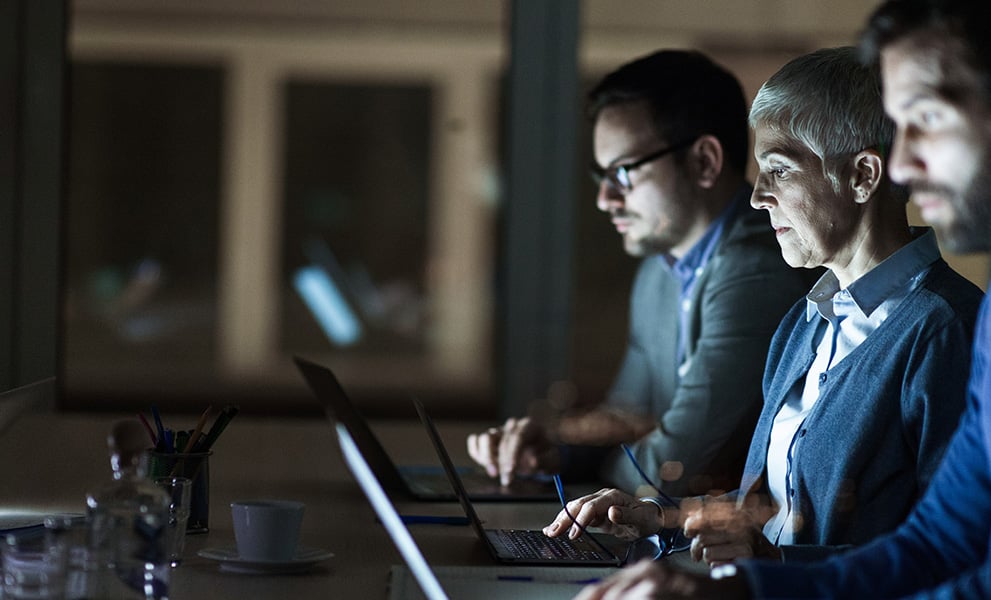 3 people in office using laptops with bright screens.