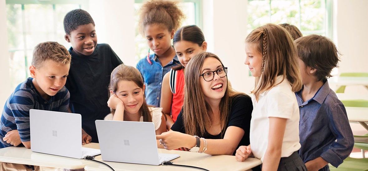 Office worker using a dual-monitor setup connected to a docking station, ergonomic keyboard, and trackball mouse at a modern workstation, with another colleague nearby.