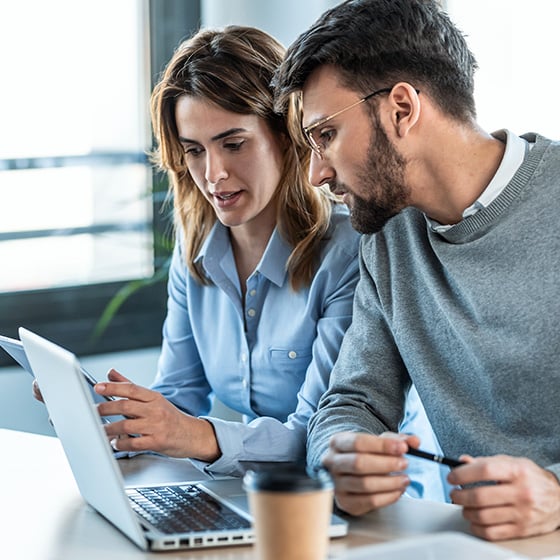 Man and woman at desk looking at laptop using a Kensington MagPro Privacy Screen Filter.