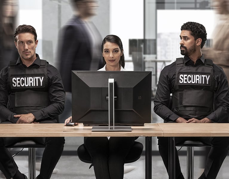Frau im Büro am Desktop mit zwei Sicherheitsbeamten neben ihr.