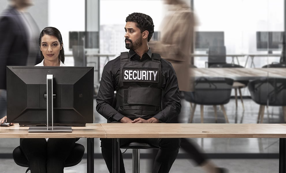 Frau im Büro am Desktop mit zwei Sicherheitsbeamten neben ihr.