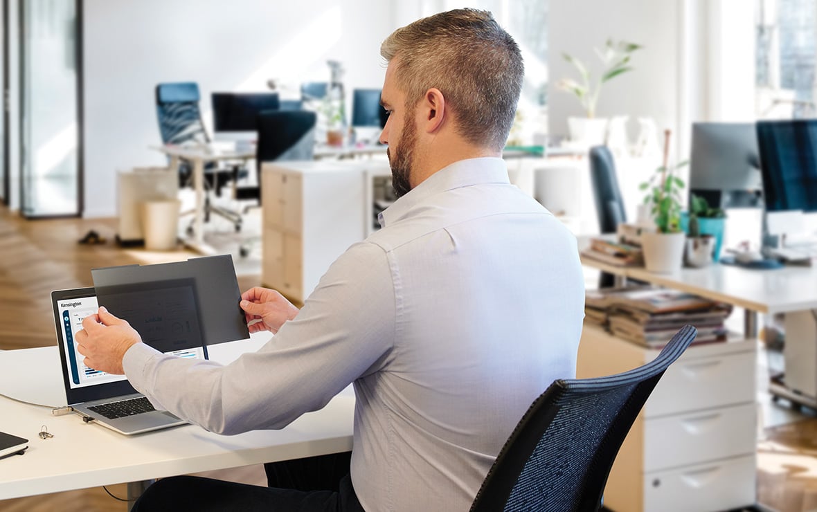 Mann am Schreibtisch, der einen Kensington-Blickschutzfilter auf seinen Laptop anbringt.