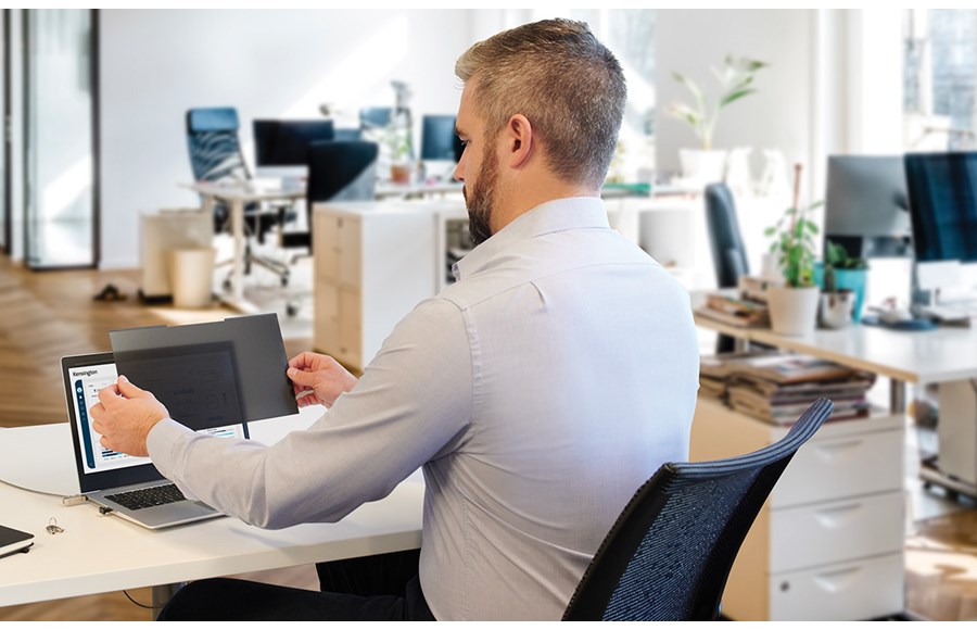 Man at desk putting a Kensington privacy screen on laptop.