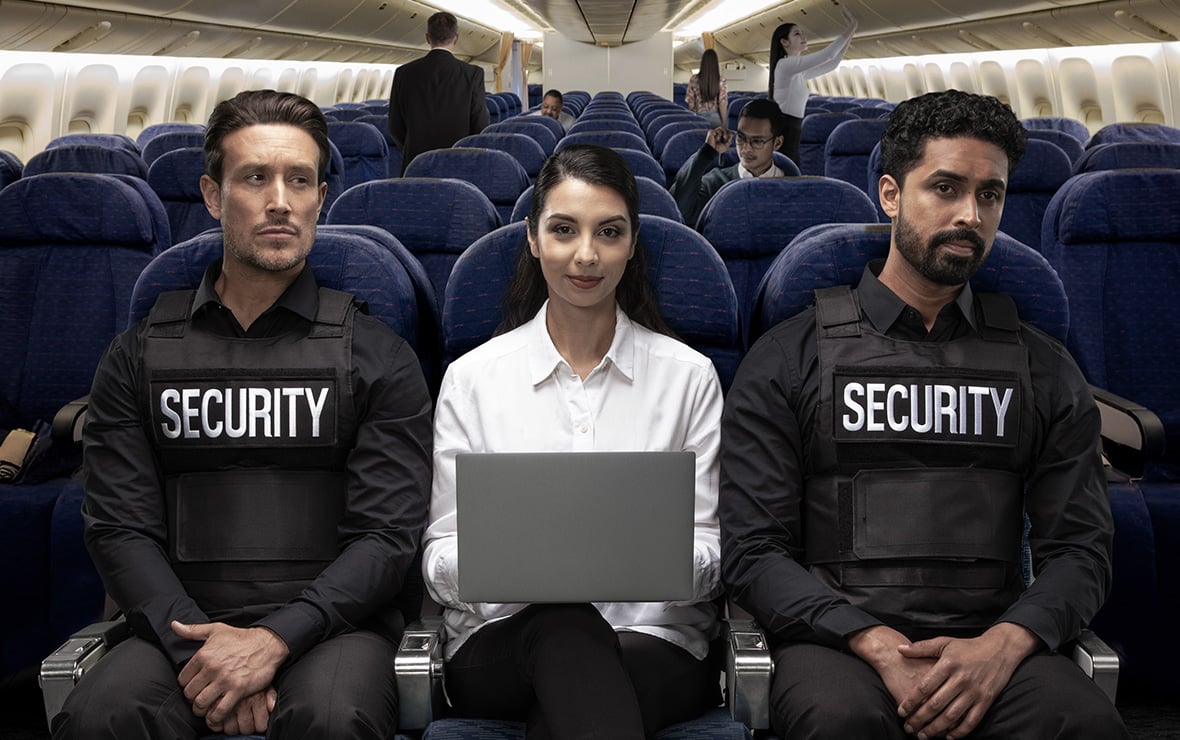 Frau im Flugzeug, die zwischen zwei Sicherheitsbeamten sitzt und einen Laptop mit einem Kensington-Blickschutzfilter mit eingeschränkter Seitenansicht verwendet.