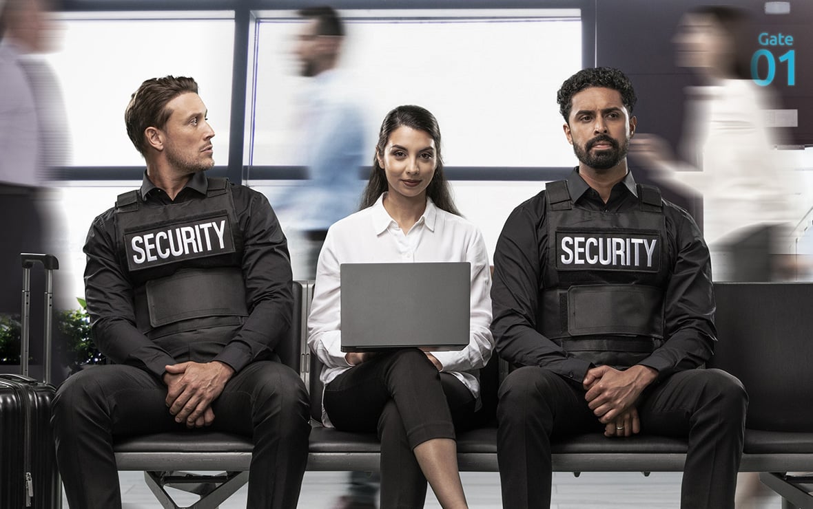 Frau auf einer Bank, die zwischen zwei Sicherheitsbeamten sitzt und ihren Laptop mit einem Kensington-Blickschutzfilter verwendet.