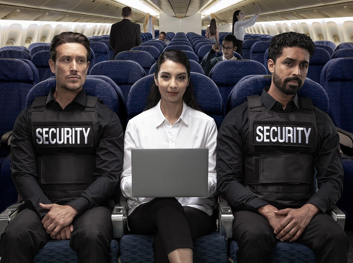 Woman on plane sitting between two security guards using laptop with Kensington privacy screen with limited side viewing.