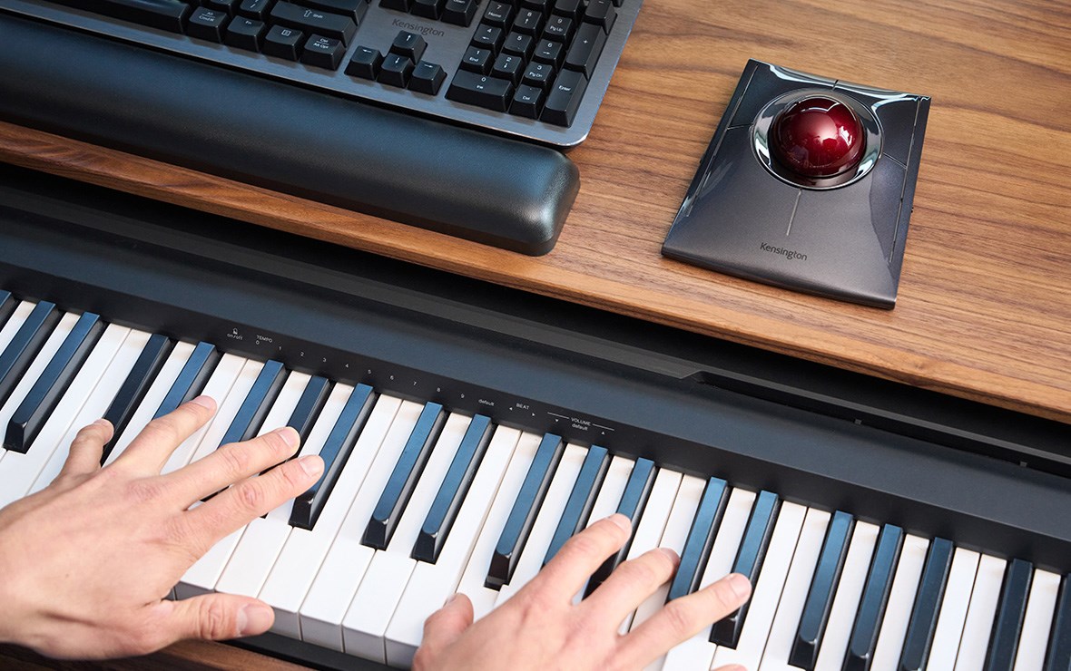 Primo piano di mani di uomo che suonano il pianoforte e scorrono le immagini con la trackball Slimblade pro.