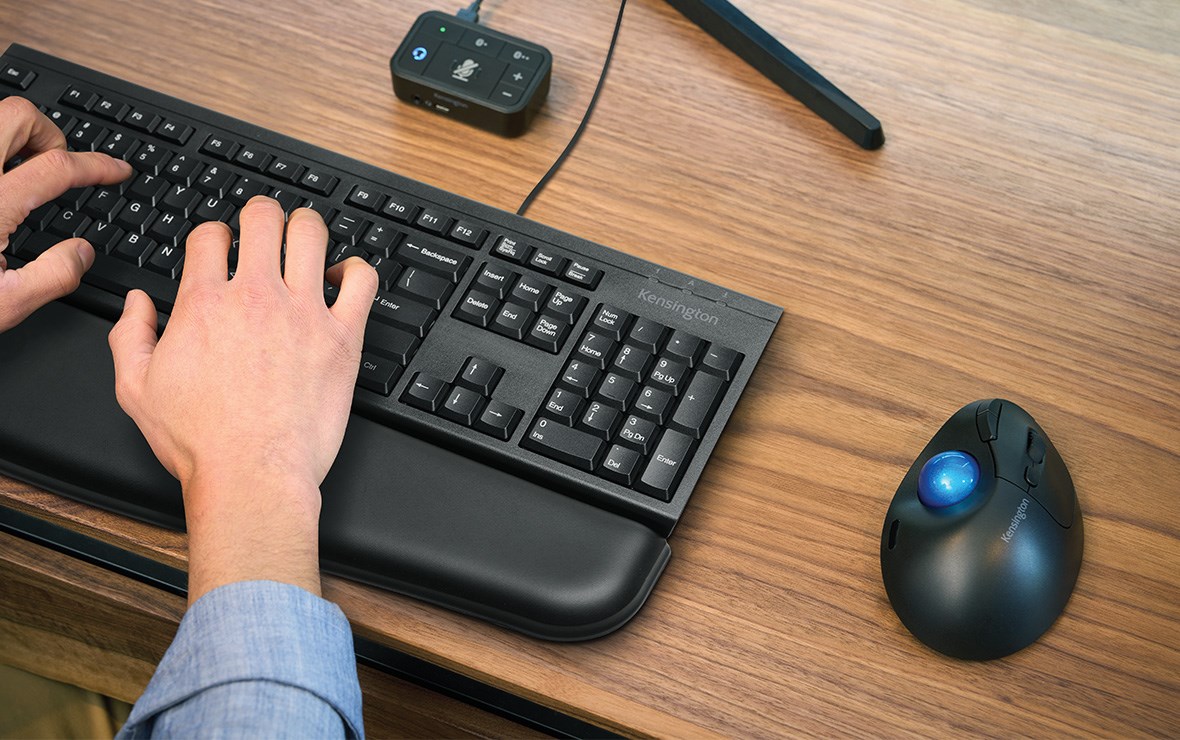 Un hombre trabajando en la oficina con varios productos de Kensington sobre su escritorio.