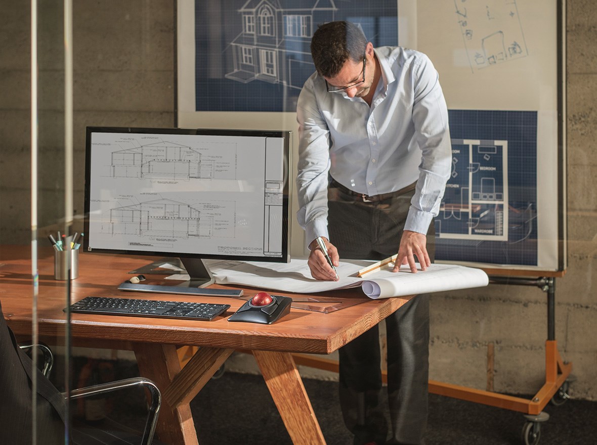 Man in the office measuring plans and the expert trackball on his desk.